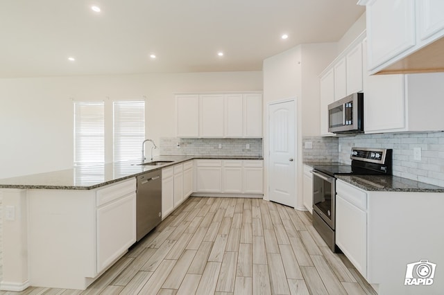 kitchen with dark stone counters, a peninsula, appliances with stainless steel finishes, and a sink