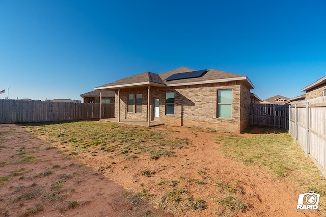 back of house featuring roof mounted solar panels, a yard, a fenced backyard, a patio area, and brick siding