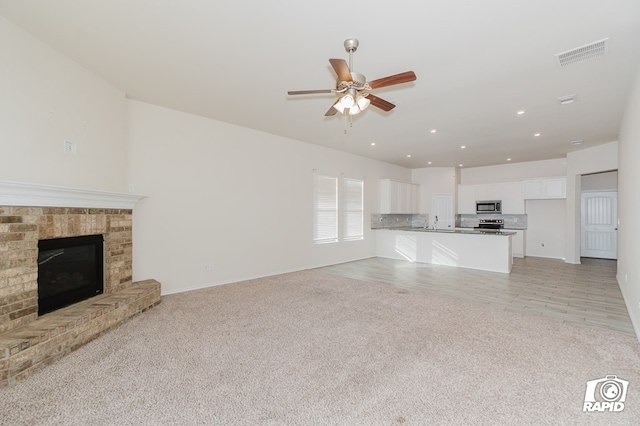 unfurnished living room featuring light colored carpet, a fireplace, a ceiling fan, and visible vents
