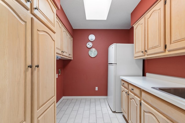 kitchen featuring light brown cabinets, freestanding refrigerator, light countertops, baseboards, and light tile patterned flooring