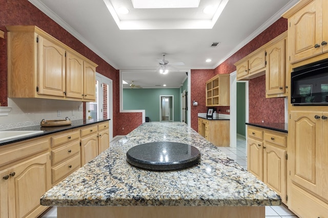 kitchen with dark stone counters, light brown cabinetry, a kitchen island, ornamental molding, and black microwave