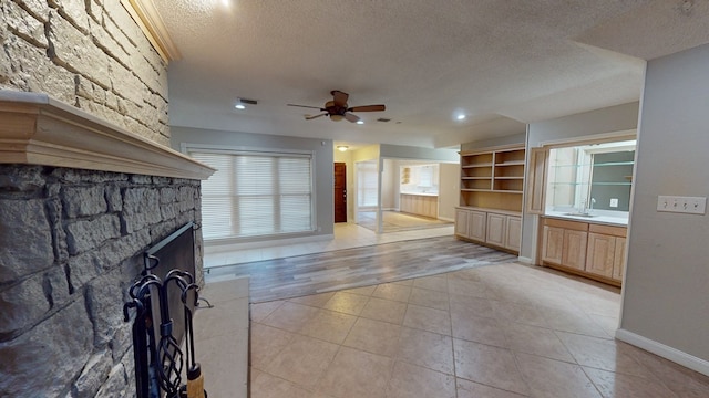 3608 Apollo Ct, Midland, TX 79707 - unfurnished living room featuring a textured ceiling, a ceiling fan, light tile patterned flooring, baseboards, and a stone fireplace