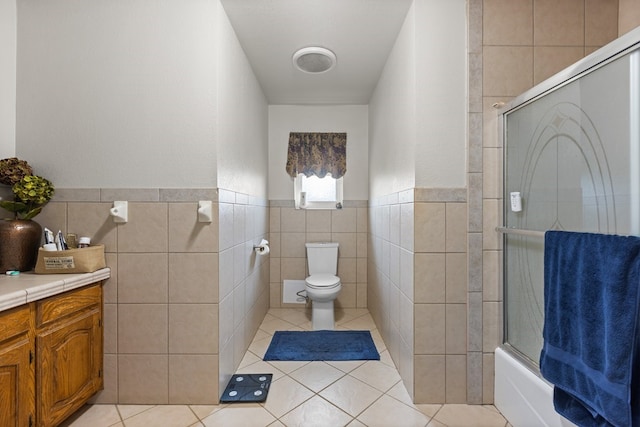 full bathroom featuring combined bath / shower with glass door, tile walls, vanity, toilet, and tile patterned floors