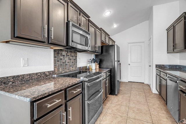 kitchen featuring appliances with stainless steel finishes, vaulted ceiling, backsplash, dark stone countertops, and dark brown cabinetry