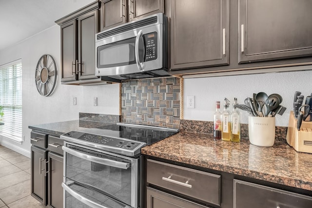 kitchen featuring stainless steel appliances, backsplash, light tile patterned floors, dark brown cabinets, and dark stone countertops