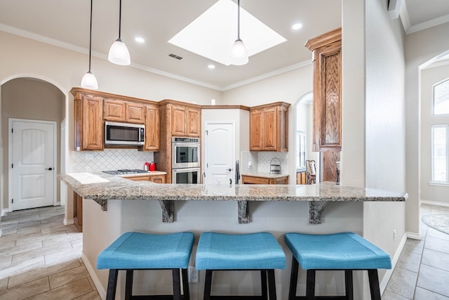 kitchen featuring a peninsula, light stone countertops, stainless steel appliances, and brown cabinetry