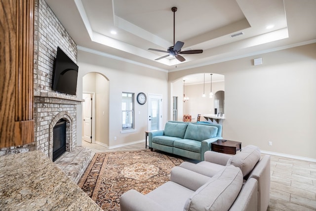 living room with arched walkways, a fireplace, visible vents, baseboards, and a raised ceiling