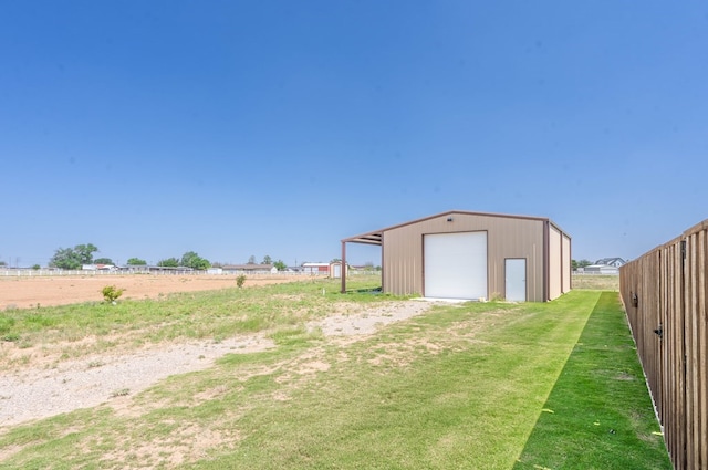 view of yard with a garage, an outbuilding, a rural view, and fence