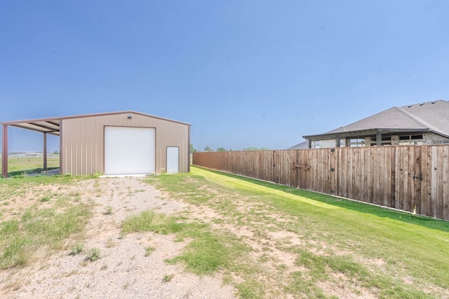 view of yard with a garage, dirt driveway, an outbuilding, and fence