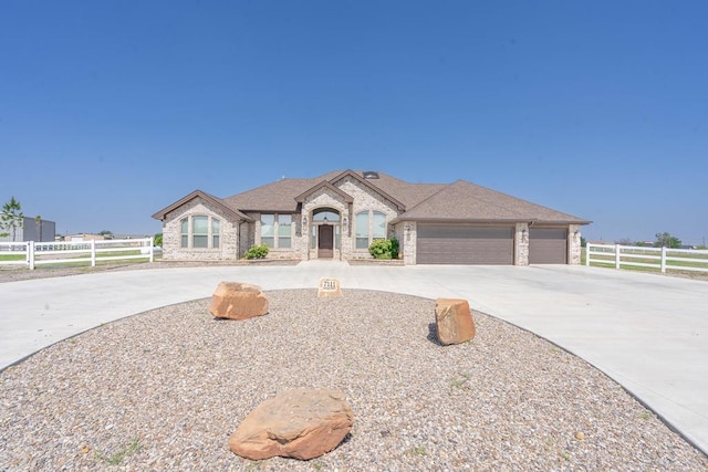 french country inspired facade featuring a garage, concrete driveway, fence, and a shingled roof