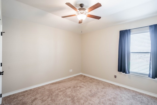 spare room featuring light carpet, a ceiling fan, a wealth of natural light, and baseboards