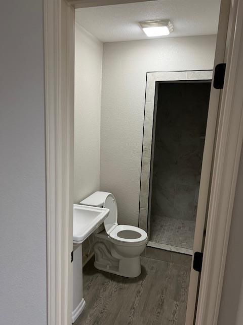 bathroom featuring toilet, wood-type flooring, and walk in shower