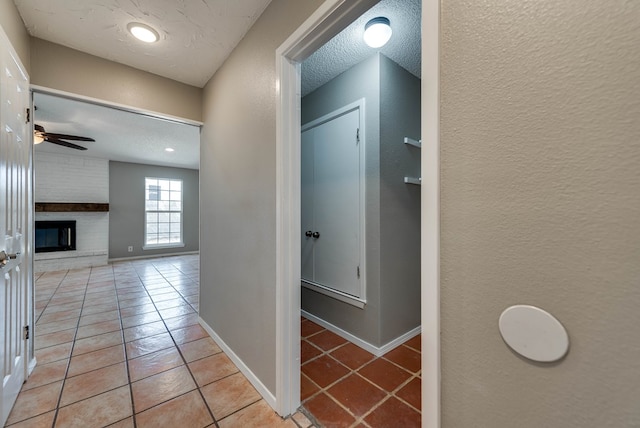 hall featuring a textured wall, light tile patterned floors, a textured ceiling, and baseboards