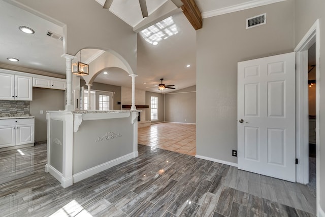 kitchen featuring ornate columns, ceiling fan, white cabinetry, arched walkways, and a high ceiling