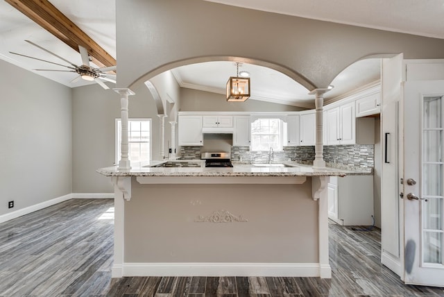 kitchen featuring stainless steel range oven, vaulted ceiling, white cabinetry, backsplash, and a kitchen bar