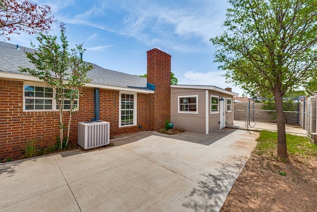 rear view of property with a gate, central AC unit, a patio area, fence, and a chimney