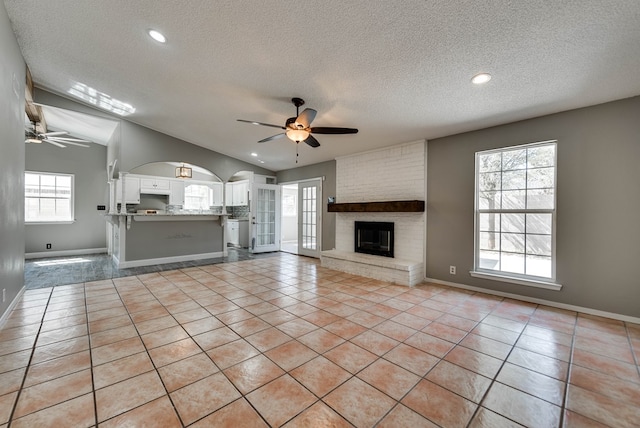 unfurnished living room with ceiling fan, a textured ceiling, a fireplace, light tile patterned flooring, and baseboards