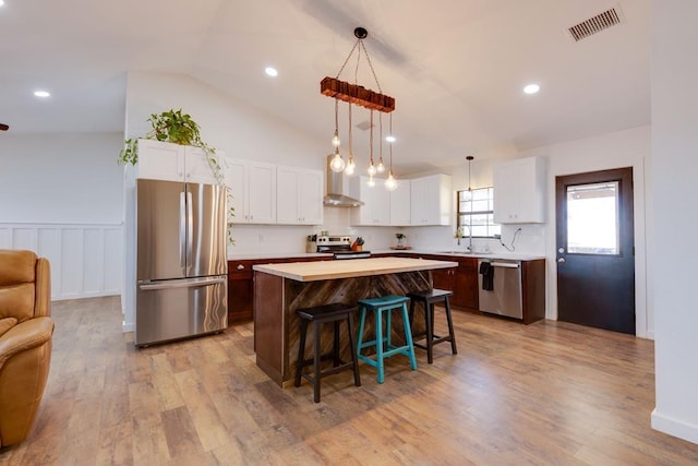 kitchen with appliances with stainless steel finishes, pendant lighting, a kitchen bar, a center island, and wall chimney range hood