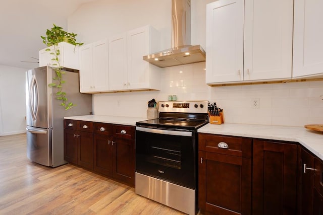 kitchen with wall chimney exhaust hood, white cabinetry, light wood-type flooring, stainless steel appliances, and backsplash