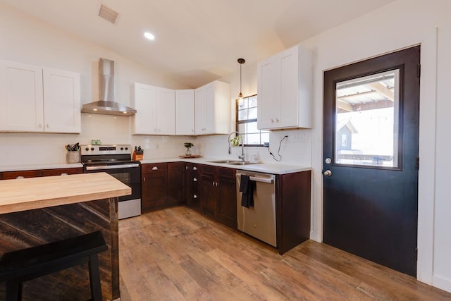 kitchen featuring appliances with stainless steel finishes, pendant lighting, white cabinetry, sink, and wall chimney range hood