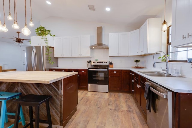 kitchen with sink, appliances with stainless steel finishes, white cabinetry, a kitchen breakfast bar, and wall chimney exhaust hood