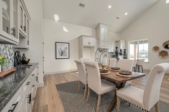 dining area with light wood-type flooring and high vaulted ceiling