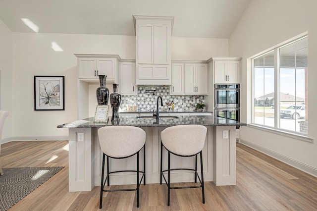 kitchen featuring white cabinets, dark stone countertops, stainless steel double oven, and sink