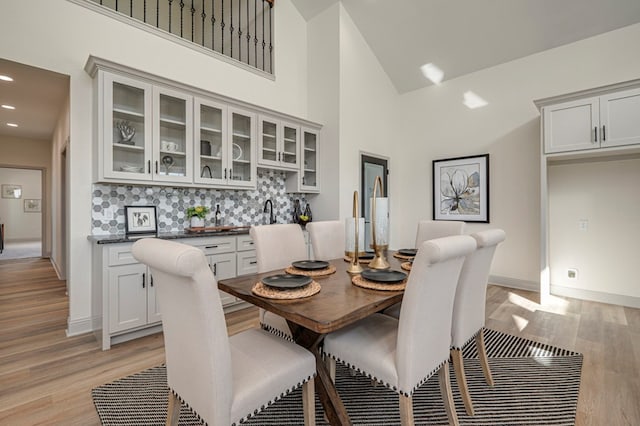 dining room featuring high vaulted ceiling and light hardwood / wood-style flooring