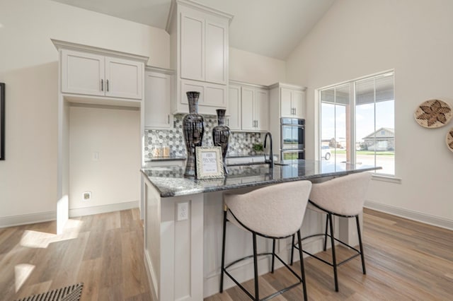 kitchen featuring white cabinets, an island with sink, double oven, and sink