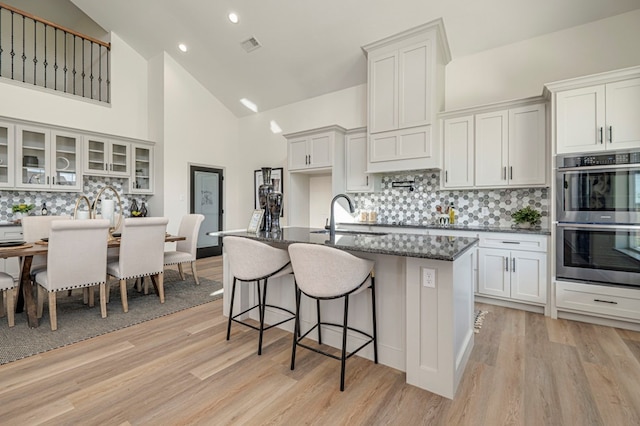 kitchen featuring dark stone counters, double oven, sink, high vaulted ceiling, and white cabinets