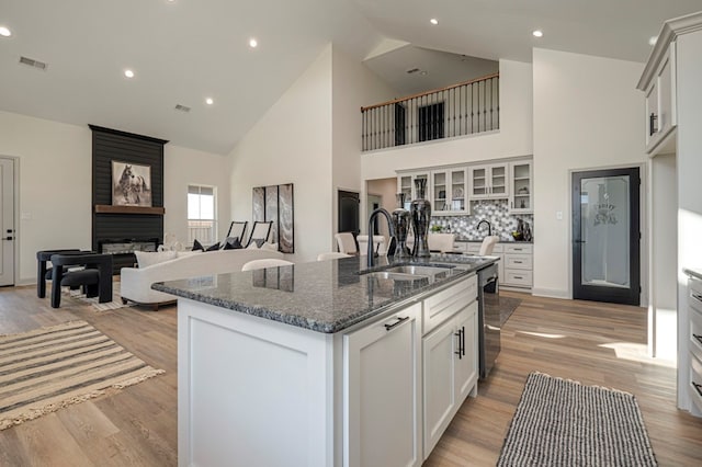 kitchen featuring white cabinetry, sink, high vaulted ceiling, light hardwood / wood-style floors, and a kitchen island with sink