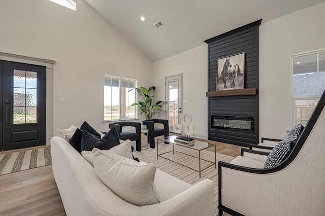 living room featuring hardwood / wood-style flooring, plenty of natural light, a large fireplace, and high vaulted ceiling