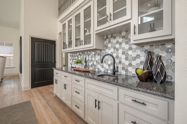 kitchen with white cabinetry, sink, tasteful backsplash, light hardwood / wood-style flooring, and dark stone counters