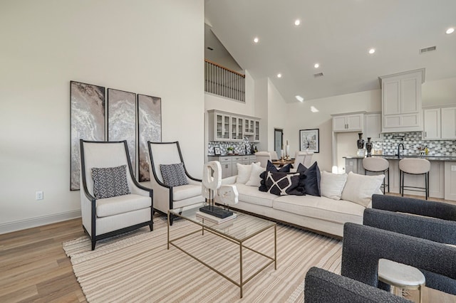 living room featuring sink, high vaulted ceiling, and light wood-type flooring