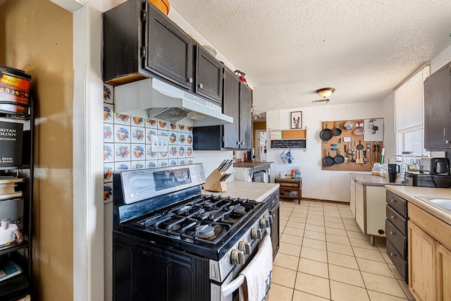 kitchen with light tile patterned floors, light countertops, under cabinet range hood, a textured ceiling, and stainless steel gas stove