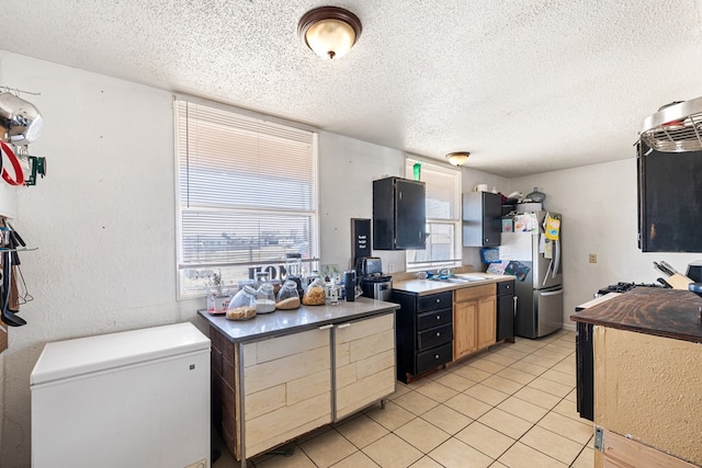 kitchen with light tile patterned floors, a textured ceiling, freestanding refrigerator, and a sink