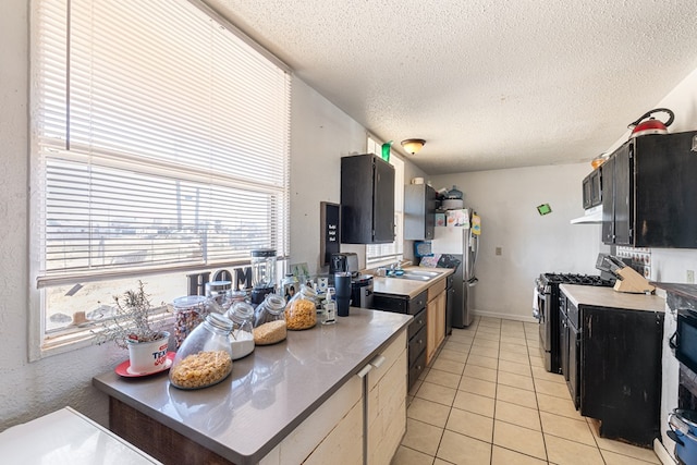 kitchen featuring light countertops, stainless steel appliances, dark cabinetry, light tile patterned flooring, and a textured ceiling