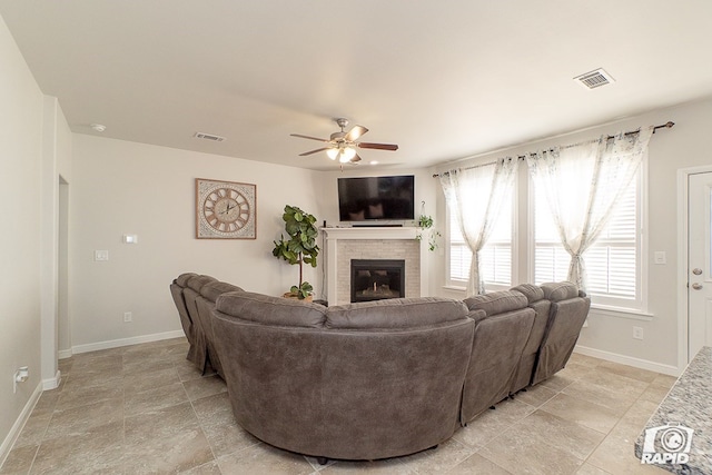 living area featuring baseboards, a glass covered fireplace, visible vents, and a ceiling fan