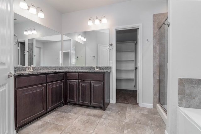 bathroom featuring double vanity, a shower stall, a walk in closet, and a sink