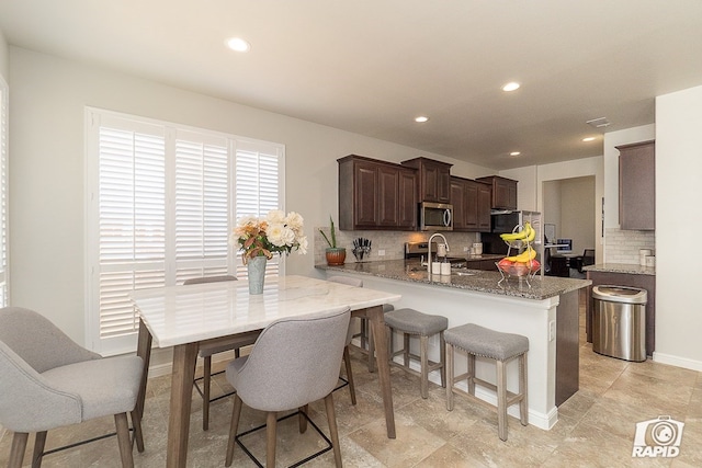 kitchen with stone countertops, stainless steel microwave, a sink, and decorative backsplash