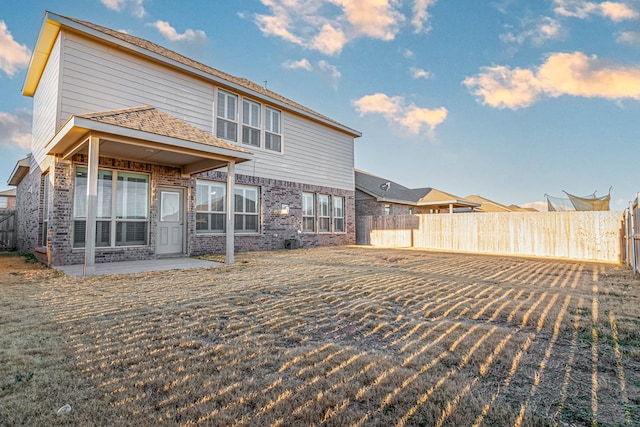 rear view of property featuring a yard, brick siding, a patio area, and a fenced backyard