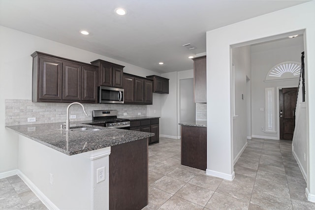 kitchen with stainless steel appliances, a sink, dark brown cabinets, dark stone counters, and tasteful backsplash