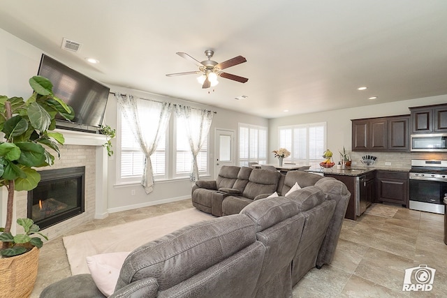 living room with baseboards, visible vents, a ceiling fan, a brick fireplace, and recessed lighting