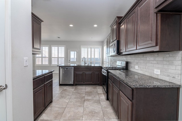 kitchen featuring stainless steel appliances, a peninsula, a sink, dark stone counters, and tasteful backsplash