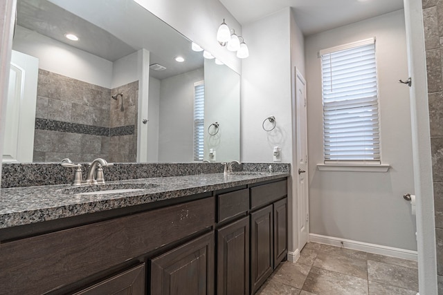 full bath featuring a sink, a tile shower, baseboards, and double vanity