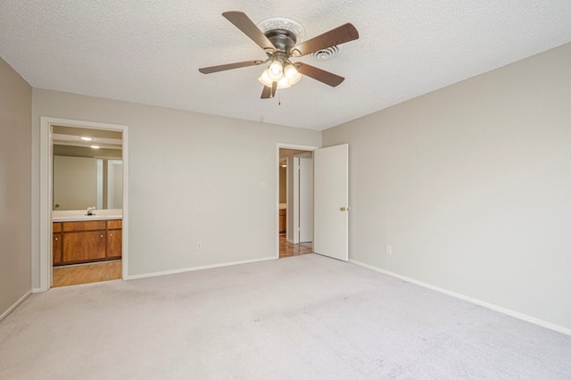 unfurnished bedroom with light carpet, a textured ceiling, ensuite bath, and baseboards