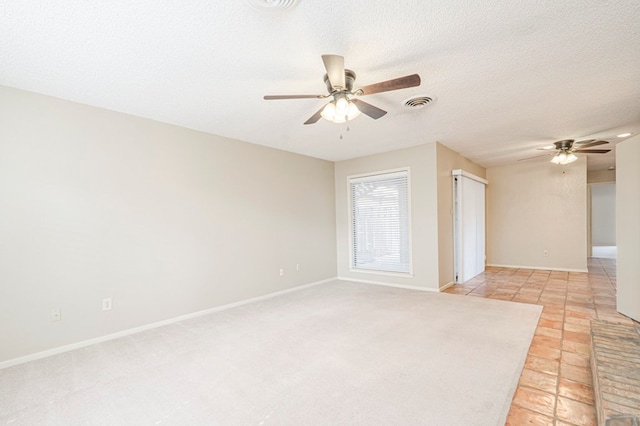 empty room with a textured ceiling, ceiling fan, visible vents, and baseboards