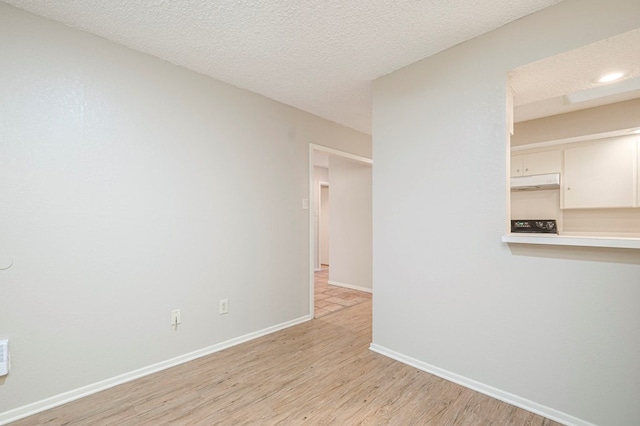 spare room with light wood-type flooring, baseboards, and a textured ceiling