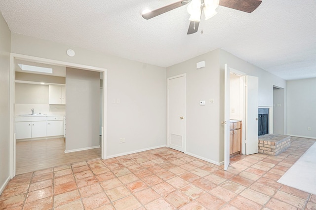 spare room featuring a brick fireplace, visible vents, a textured ceiling, and baseboards