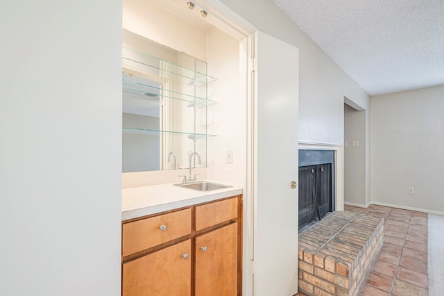 bar with a textured ceiling, baseboards, a fireplace with raised hearth, and a sink